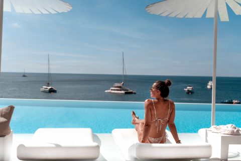 Woman sunbathing by a luxury infinity pool with ocean view and yachts in the background
